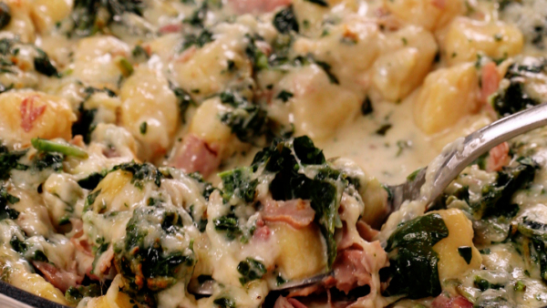 a fork scooping up Cheesy Spinach and Ham gnocchi in a skillet