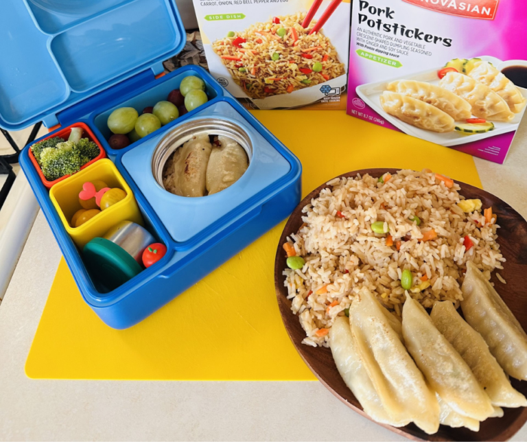 Opened lunchbox next to a plate of fried rice and potstickers
