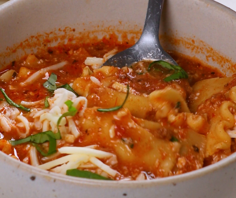 A small silver spoon mixing a bowl of lasagna soup